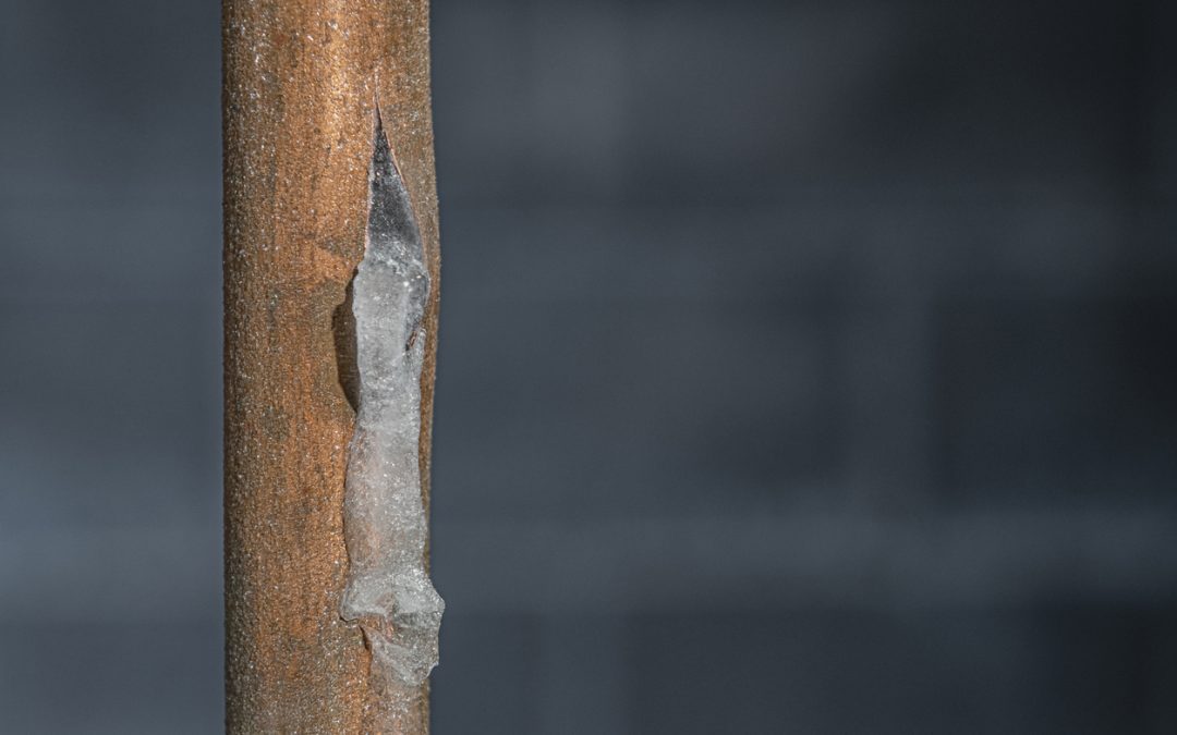 A close-up of a frozen copper pipe covered in frost against a basement wall