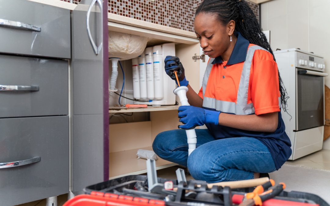 plumber in uniform fixing kitchen sink she is sitting on the floor in kitchen and fixing pipe